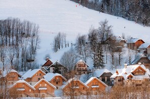 A snowy village with wooden houses, a ski slope, and a clear sky. - Proche des pistes | Piscine int/ext | Duplex (Saint-Colomban-des-Villards)