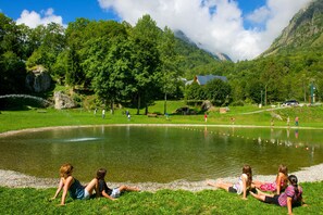 A lake with people relaxing on the grass, a picnic area, and a mountain in the background. - Proche des pistes | Piscine int/ext | Duplex (Saint-Colomban-des-Villards)