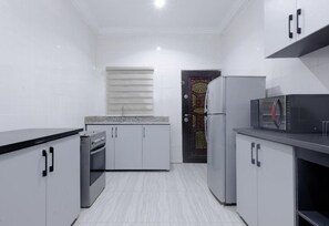A kitchen with white cabinets, a microwave, and a refrigerator. - The Capital Apartments (Abuja)
