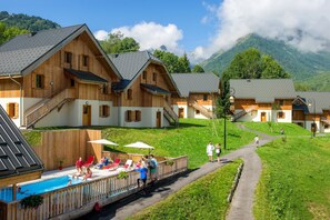 Ein Chalet aus Holz mit Schwimmbeckenbereich, umgeben von üppiger Vegetation und Bergen.