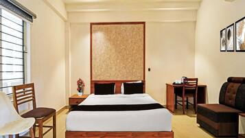 Hotelkamer met een bed, bureau, stoel, bank, plafondventilator en raam met jaloezieën.