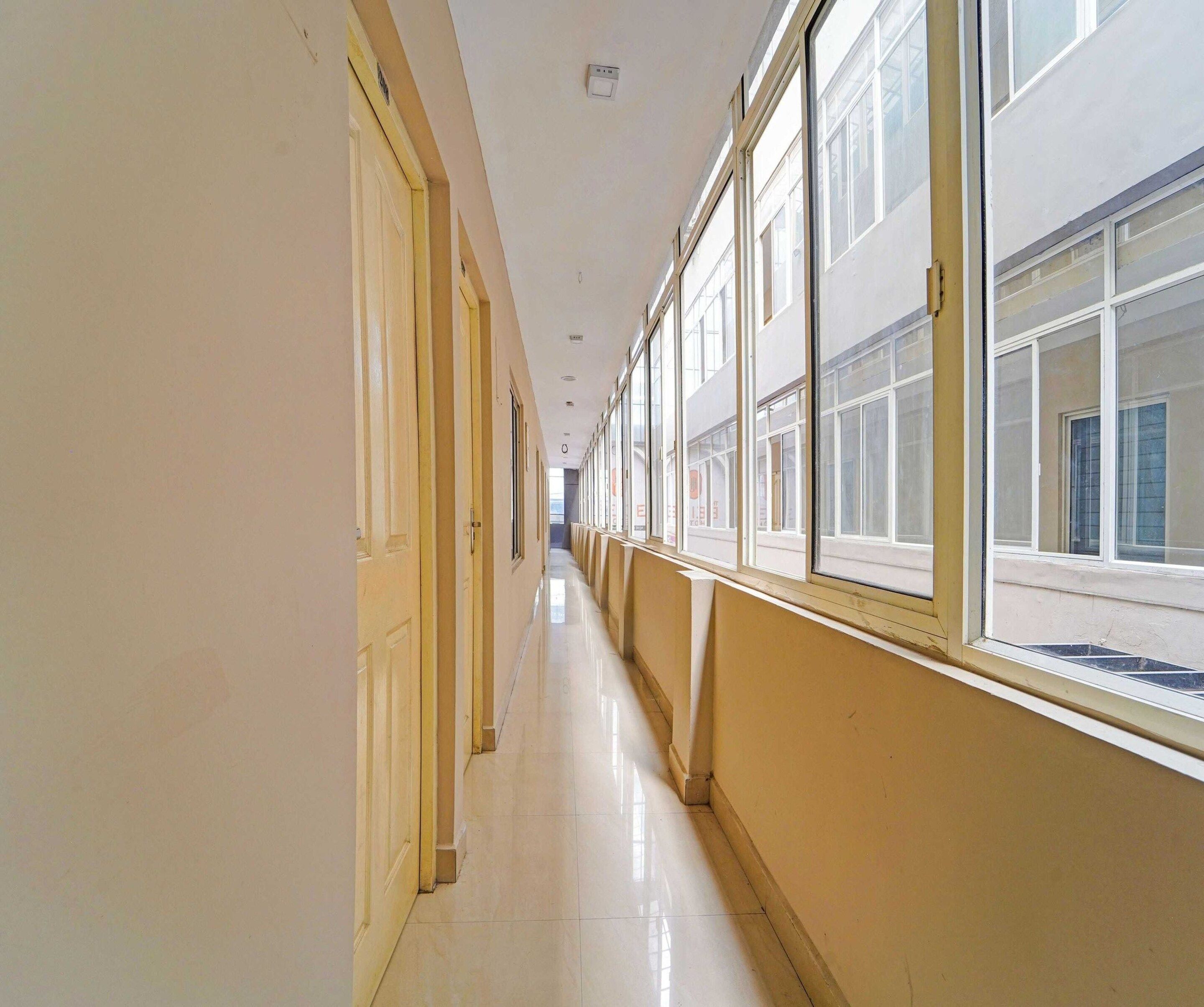 A long, narrow hallway with doors on one side and windows on the other, leading to a bright interior space.