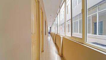 A long, narrow hallway with doors on one side and windows on the other, leading to a bright interior space.