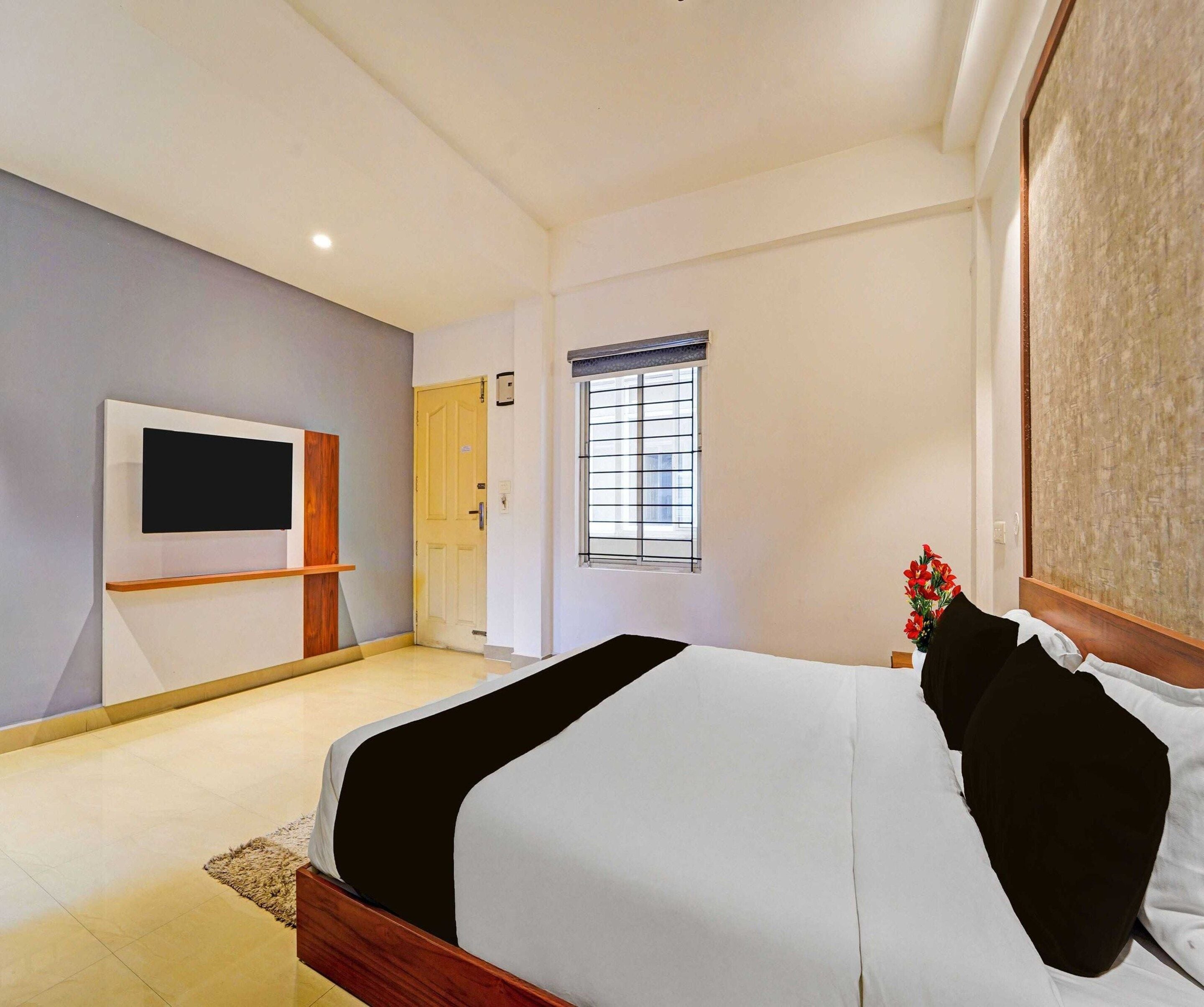 A hotel room with a bed, a TV, a window with bars, and a door.