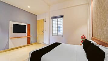 A hotel room with a bed, a TV, a window with bars, and a door.