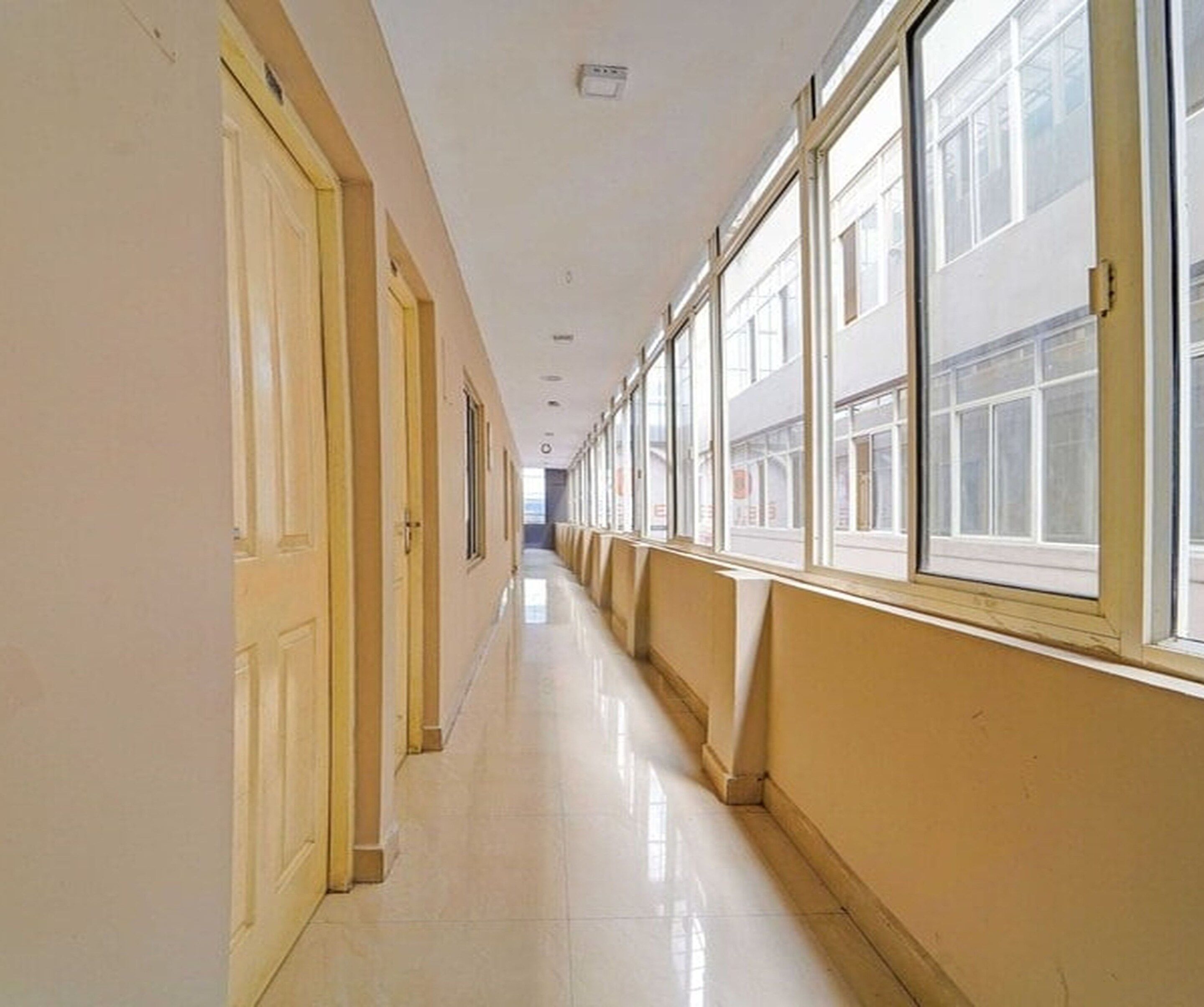A long, narrow hallway with doors on one side and windows on the other, leading to an open area.