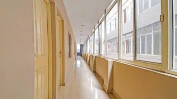 A long, narrow hallway with doors on one side and windows on the other, leading to an open area.