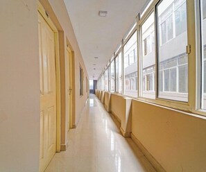 A long, narrow hallway with doors on one side and windows on the other, leading to an open area. - Classic Mattuthavani Bus Terminal Madurai (Madurai)