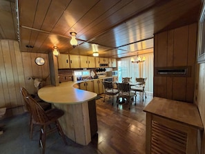 A kitchen with wooden cabinets, a central island, bar stools, and a dining area with chairs.