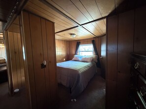 A wooden-paneled room with a bed, a window with curtains, and a ceiling fan.