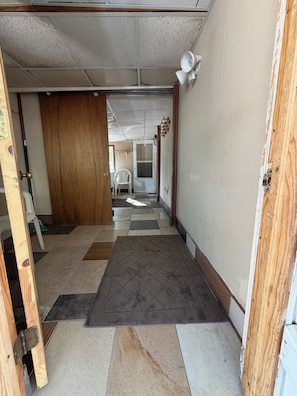 A hallway with a checkered floor, a wooden door, and a white chair in the distance.