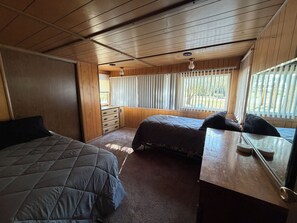 A bedroom with two beds, a dresser, and a window with blinds.
