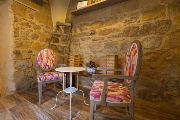 A rustic stone wall interior with a wooden table and two patterned chairs.