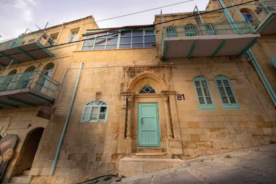 Un bâtiment historique dont la façade est ornée d’un grand chiffre « 81 », doté d’une entrée centrale en arc de cercle et de balcons avec des garde-corps verts.
