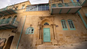 Un bâtiment historique dont la façade est ornée d’un grand chiffre « 81 », doté d’une entrée centrale en arc de cercle et de balcons avec des garde-corps verts.