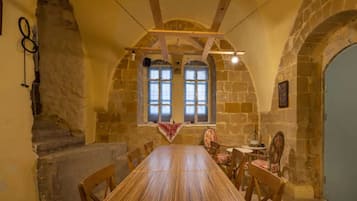 Une salle à manger avec une longue table en bois, des murs en pierre et des fenêtres en arc de cercle.