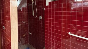 Ein Badezimmer mit roten Fliesenwänden, einer Duschkabine aus Glas und einem weißen Handtuchhalter.