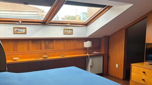 Ein Schlafzimmer mit Dachfenster, Holzvertäfelung, einem Bett mit blauer Bettdecke, einem Nachttisch und einer Kommode.