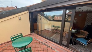 Eine Terrasse mit Glastür zu einem Zimmer, grünen Stühlen und einem Tisch.