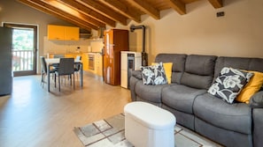 A modern living room with a grey sofa, a dining area with a table and chairs, and a kitchen with wooden cabinets and appliances. - Abri Douillet - Cozy Apartment with Private Parking in Saint-Marcel (Saint-Marcel)