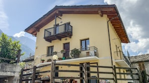 A two-story building with a balcony, a wooden fence, and a mountain backdrop. - Abri Douillet - Cozy Apartment with Private Parking in Saint-Marcel (Saint-Marcel)