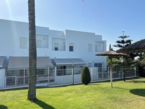 A modern white building with a flat roof, a fenced outdoor area, and a thatched structure. - Luz de Conil: Style and comfort just steps from the beach. (Conil de la Frontera)