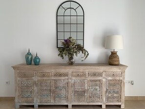 A decorative wooden cabinet with intricate carvings, a vase with flowers, and a lamp on top. - Luz de Conil: Style and comfort just steps from the beach. (Conil de la Frontera)
