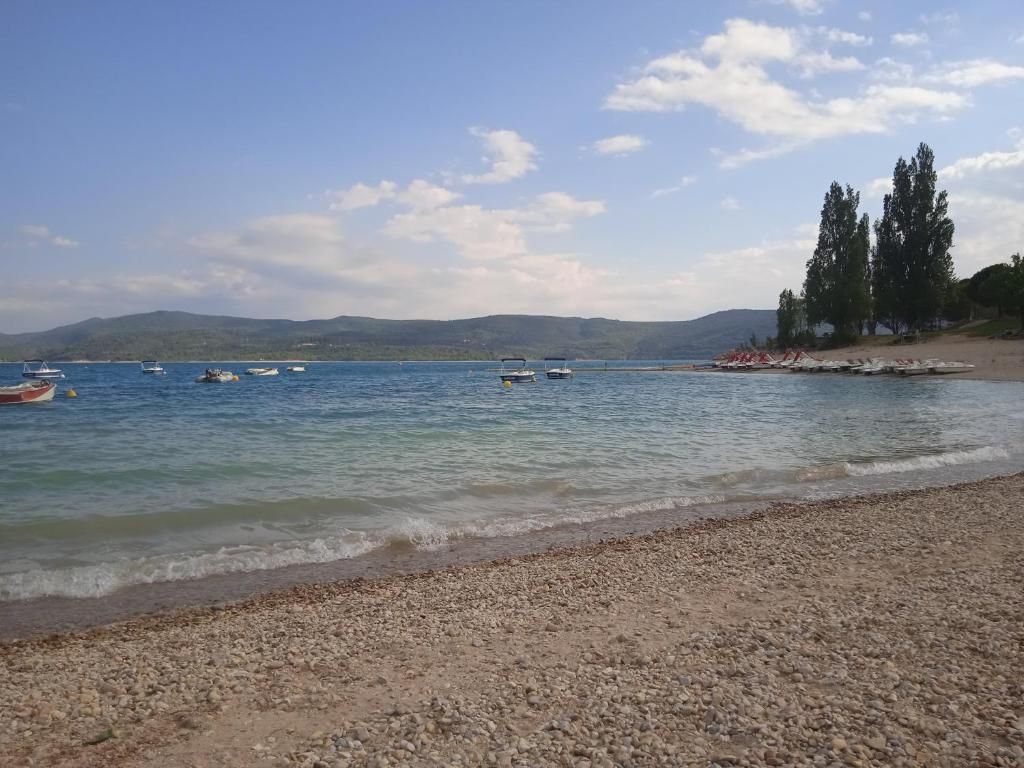 Een kiezelstrand met rustig water, boten en heuvels in de verte.