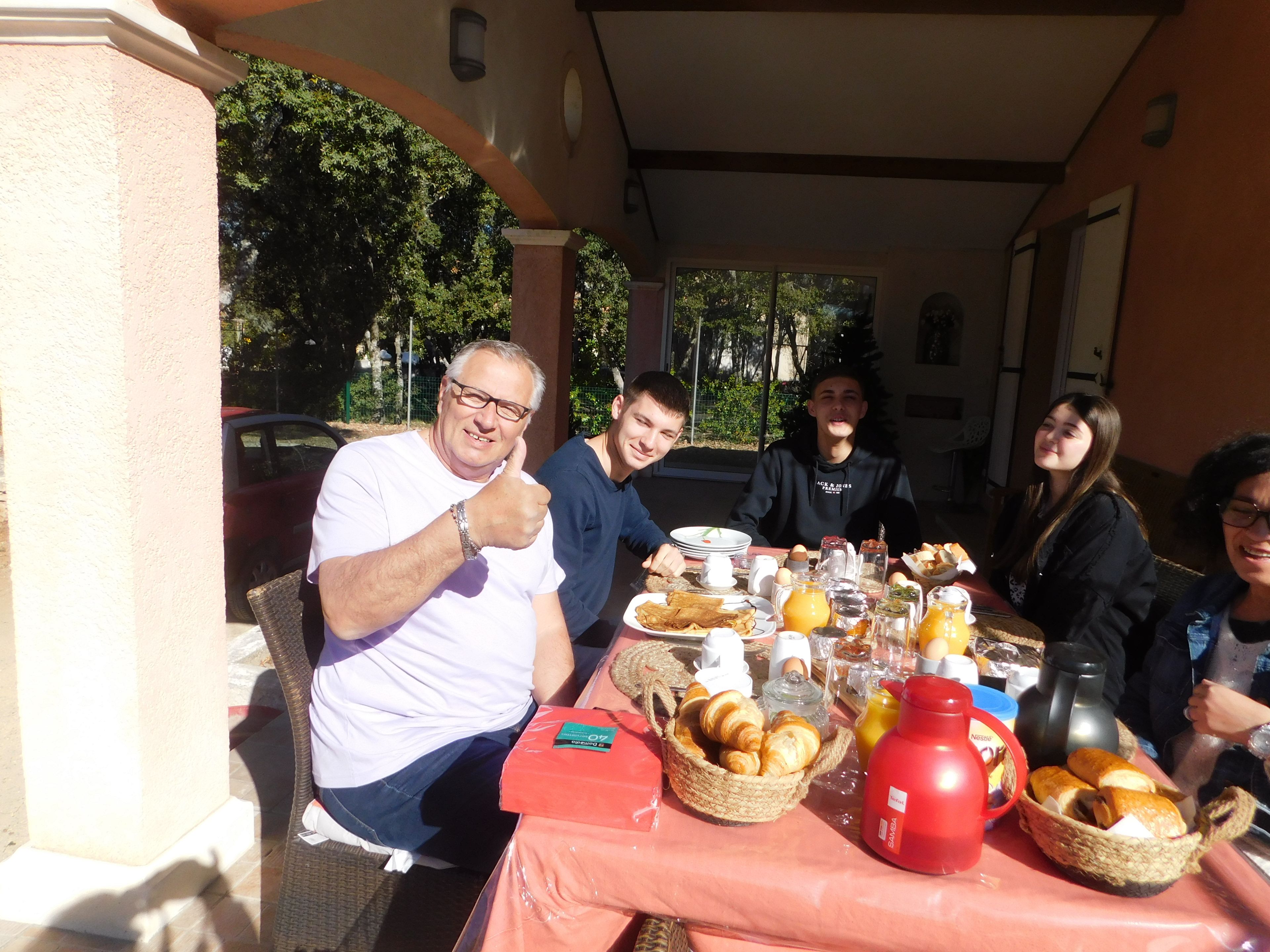 Un gruppo di persone sedute a un tavolo all'aperto, con cibi e bevande per la colazione.