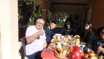 Un gruppo di persone sedute a un tavolo all'aperto, con cibi e bevande per la colazione.