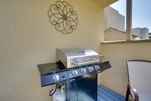 Ein Gasgrill mit vier Brennern und einem Seitenbrenner, auf einem Balkon mit Blick auf Gebäude.