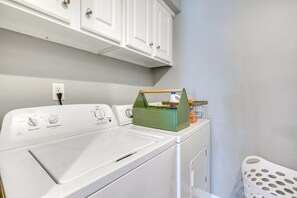 Un espace buanderie avec un lave-linge et un sèche-linge à chargement frontal, un panier vert posé sur le sèche-linge et un panier à linge blanc sur la droite.