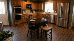 Cozinha moderna com armários de madeira, eletrodomésticos de aço inoxidável e um espaço de jantar com mesa e cadeiras.