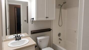 A bathroom with a white sink, mirror, cabinet, toilet, and shower.