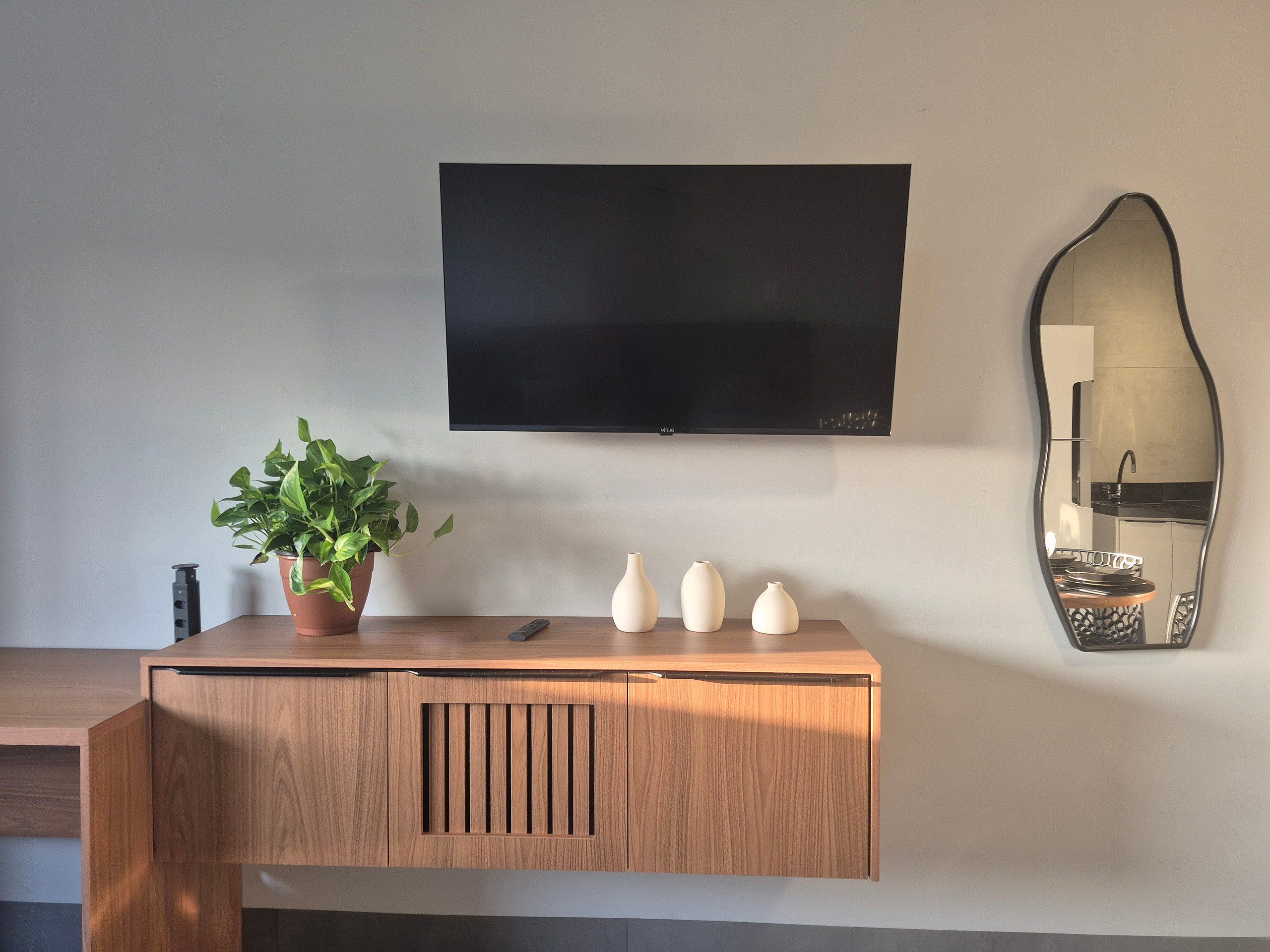 Une console en bois ornée d’une plante en pot, de trois vases et d’un téléviseur à écran plat fixé au mur.