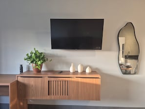 Une console en bois ornée d’une plante en pot, de trois vases et d’un téléviseur à écran plat fixé au mur.