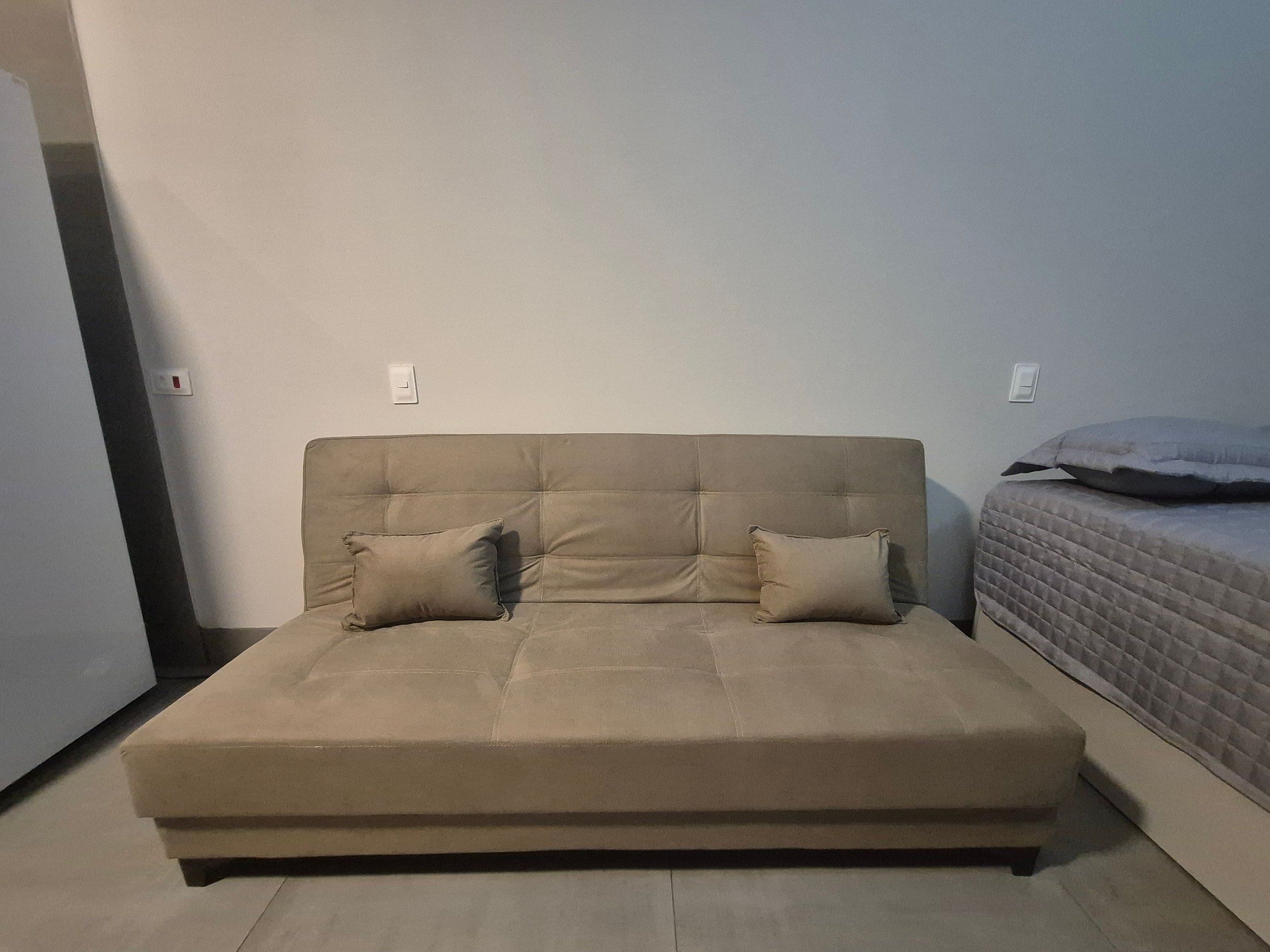 A neutral-toned sofa with two cushions, positioned against a plain wall with two light switches.