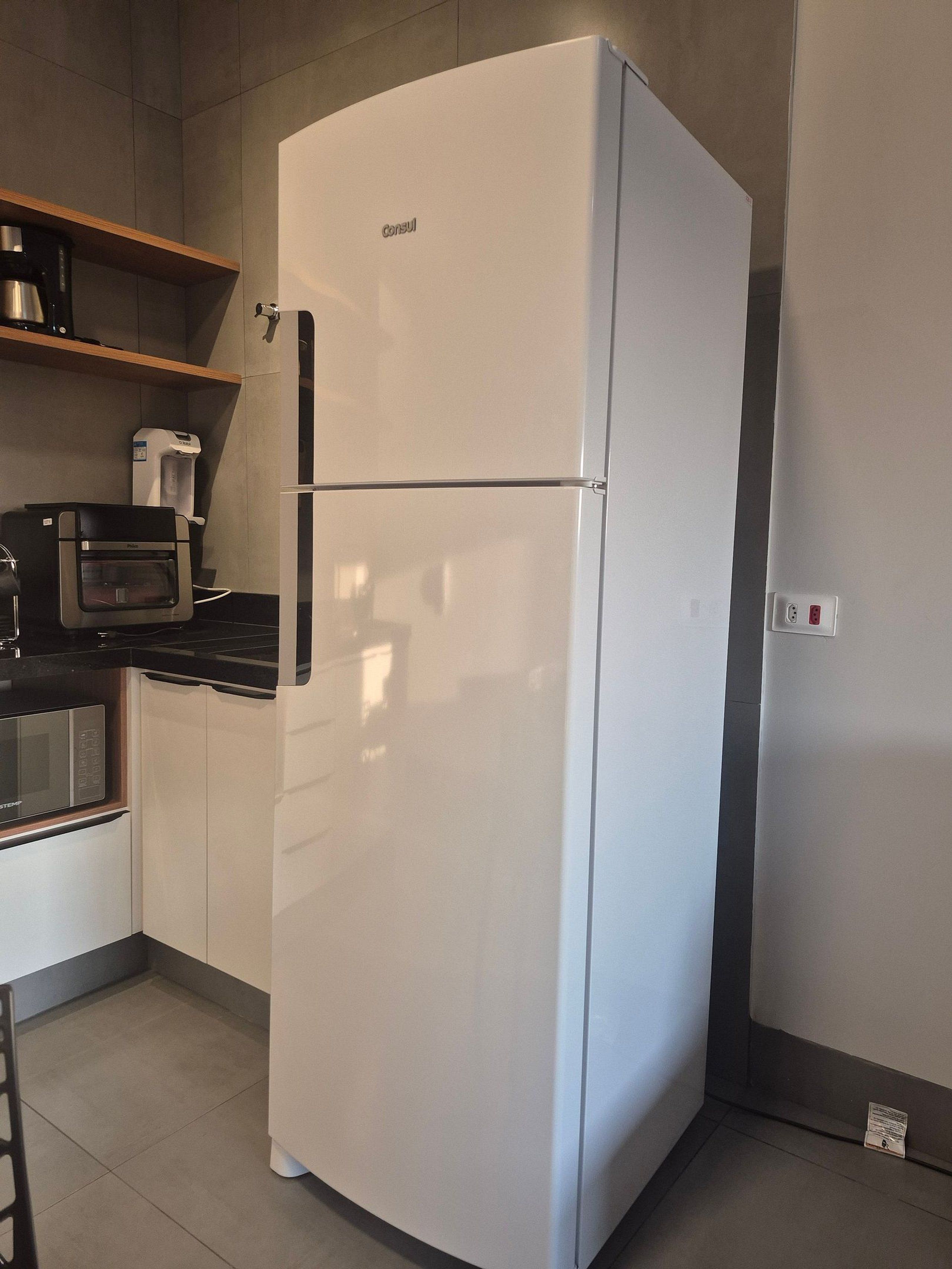 A compact kitchen with a white refrigerator, a microwave, and a coffee machine on a black countertop.