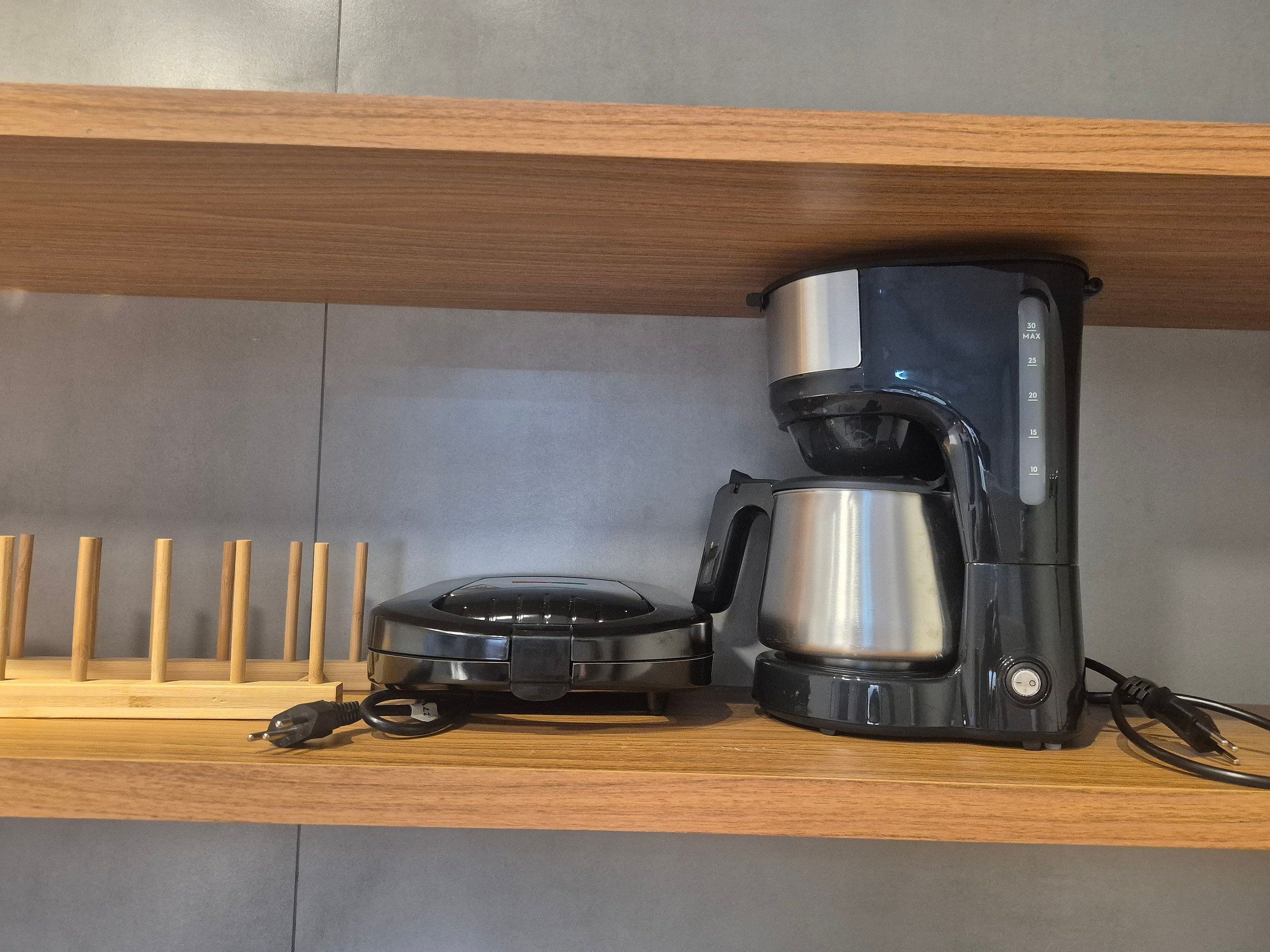 A coffee maker on a shelf with a wooden tray and a black coffee pot.