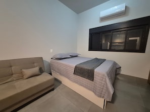 Un dormitorio con cama, sofá, aire acondicionado y ventana con persianas.