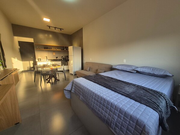 A modern bedroom with a large bed, a sofa, and a dining area with a table and chairs.