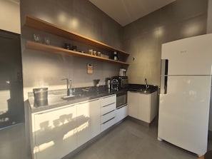 Una cocina moderna con refrigerador, horno, cafetera y un estante con utensilios de cocina.