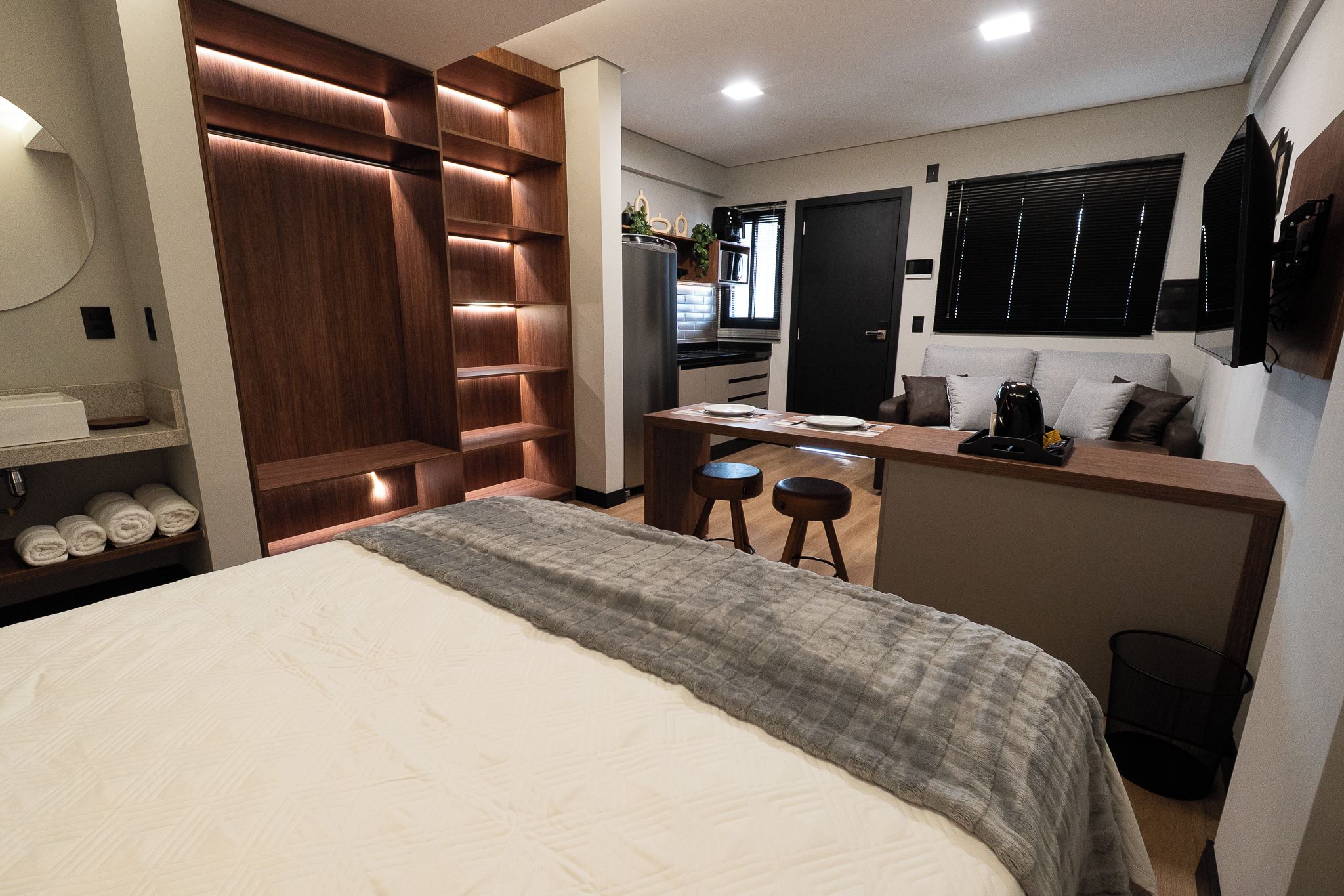 A compact bedroom with a bed, a built-in wardrobe, a kitchenette, and a seating area.