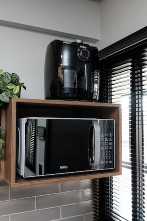 A kitchen with a black coffee maker and a microwave on a wooden shelf. - Iguassu Pointe Suites (Foz do Iguaçu)