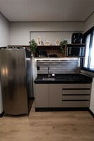 Cozinha moderna com geladeira de aço inoxidável, bancada preta e micro-ondas.