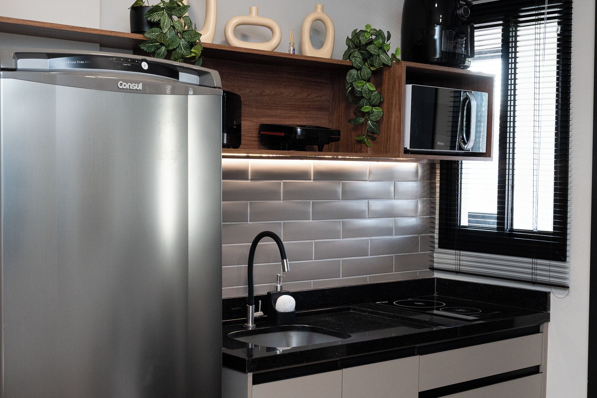 A modern kitchen with a stainless steel refrigerator, a black sink, and a built-in microwave.