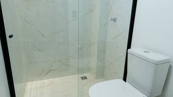 Un baño con ducha de vidrio, inodoro blanco y lavamanos blanco.