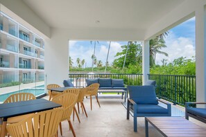Ein Balkon mit Sitzgelegenheit, einem Pool und Blick auf Palmen.