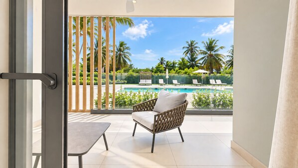 Ein Balkon mit Blick auf einen Swimmingpool, Liegestühle und Palmen.