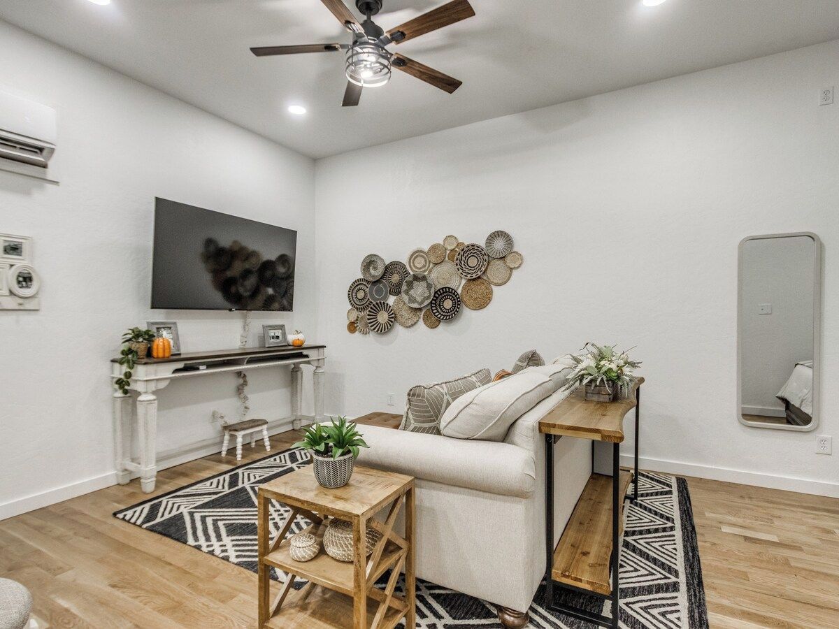 A modern living room with a sofa, a coffee table, a TV mounted on the wall, and a ceiling fan.